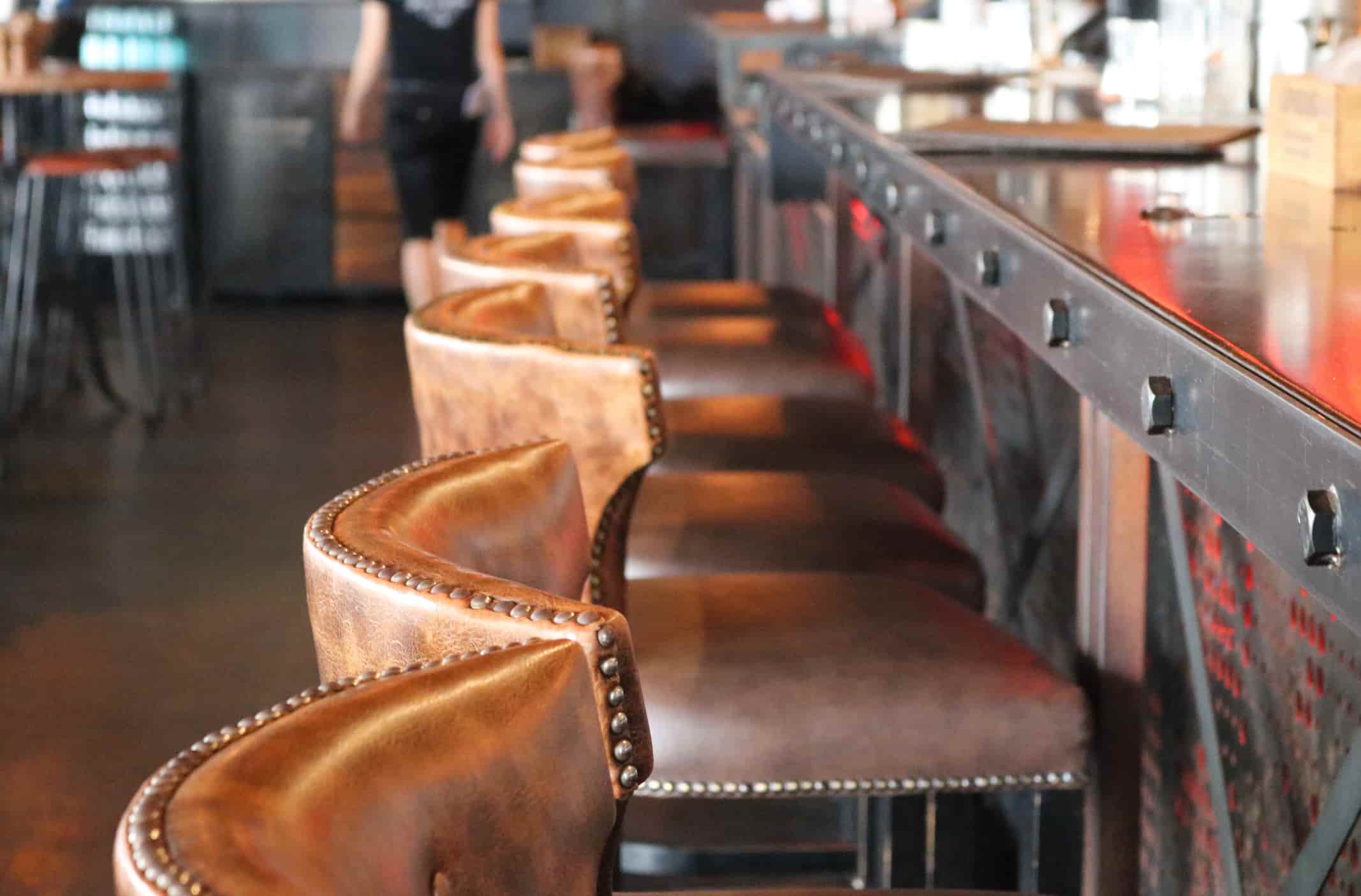 Leather bar stools with metal details arranged along a restaurant bar counter for commercial hospitality use