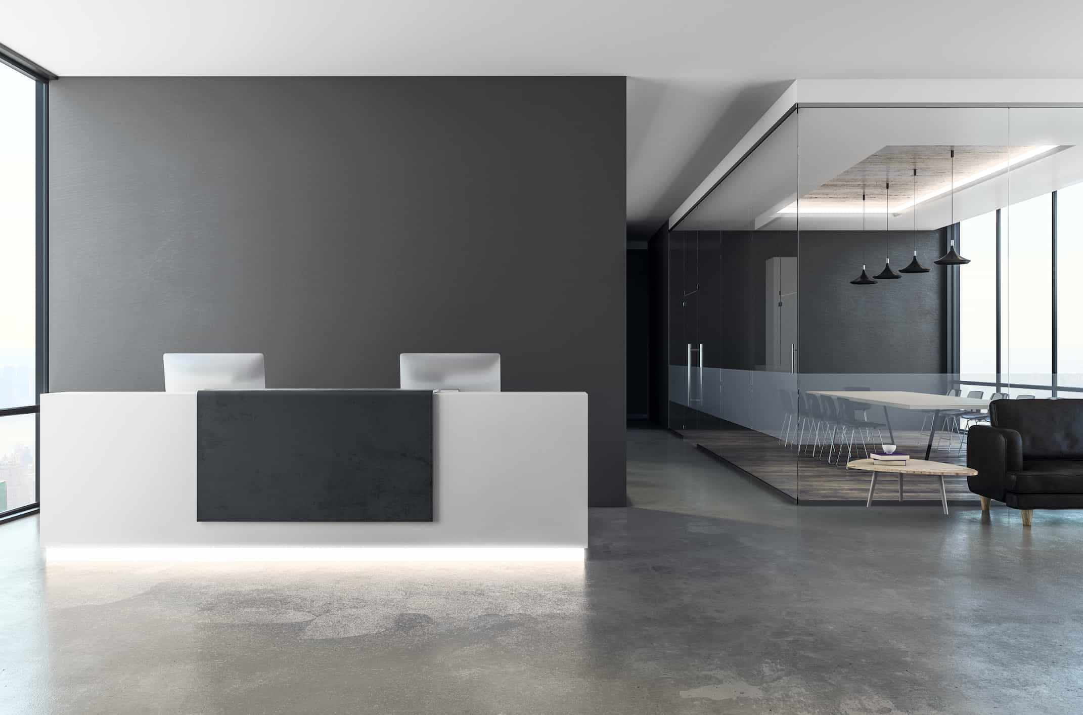 Modern hotel lobby featuring a minimalist reception desk and a glass-enclosed meeting area.