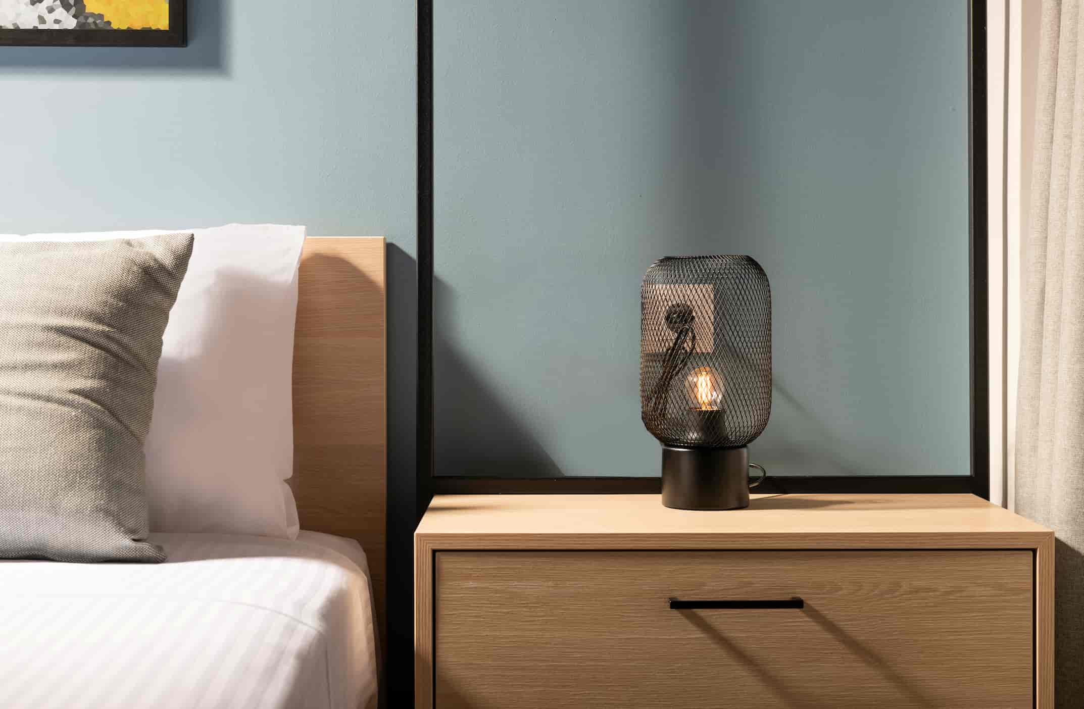 Hotel nightstand manufacturer in Turkey showing modern wooden bedside table with drawer and decorative lamp.