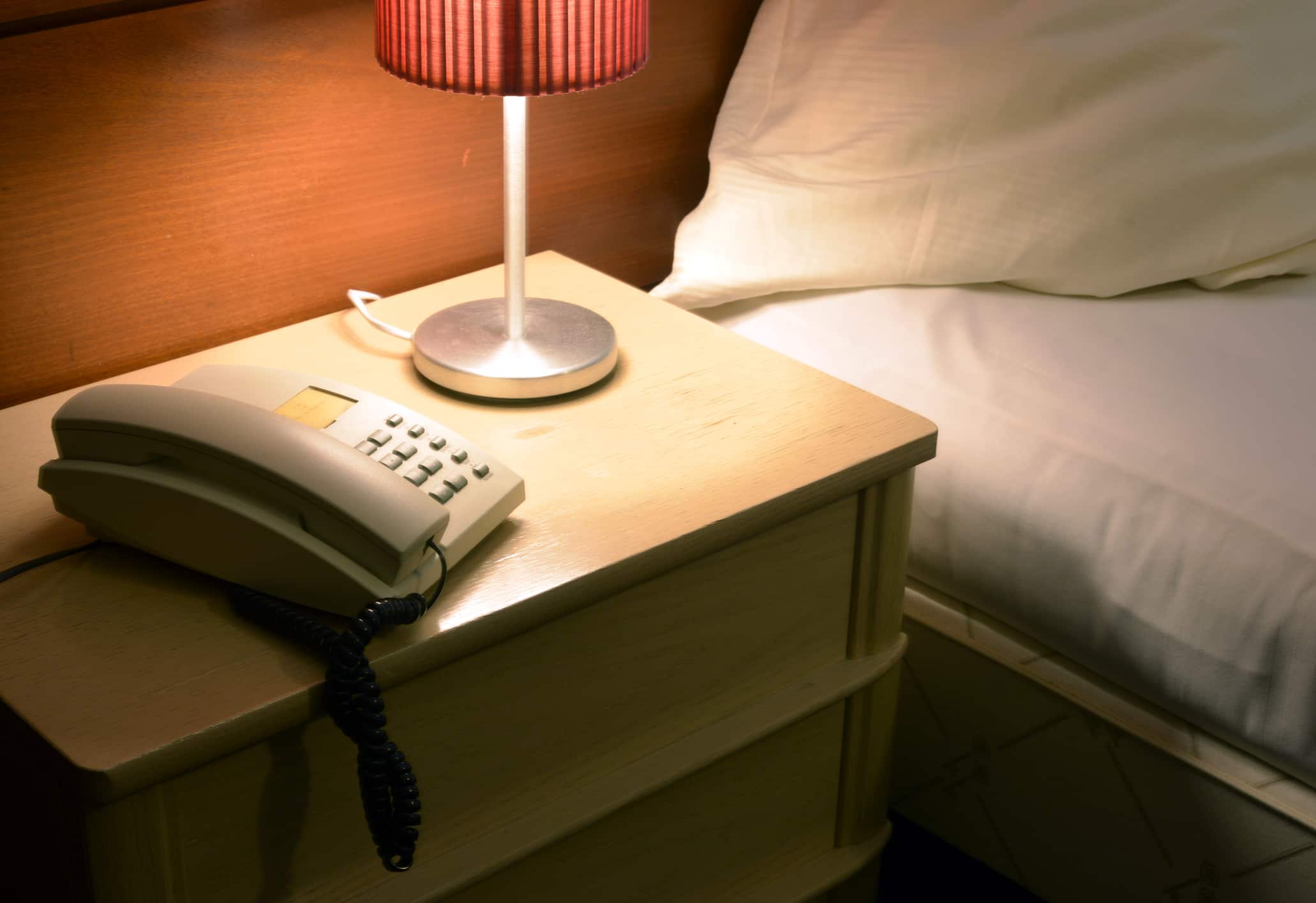 Hotel nightstand manufacturer in Turkey displaying wooden bedside table with drawer, lamp and telephone for hotel rooms.