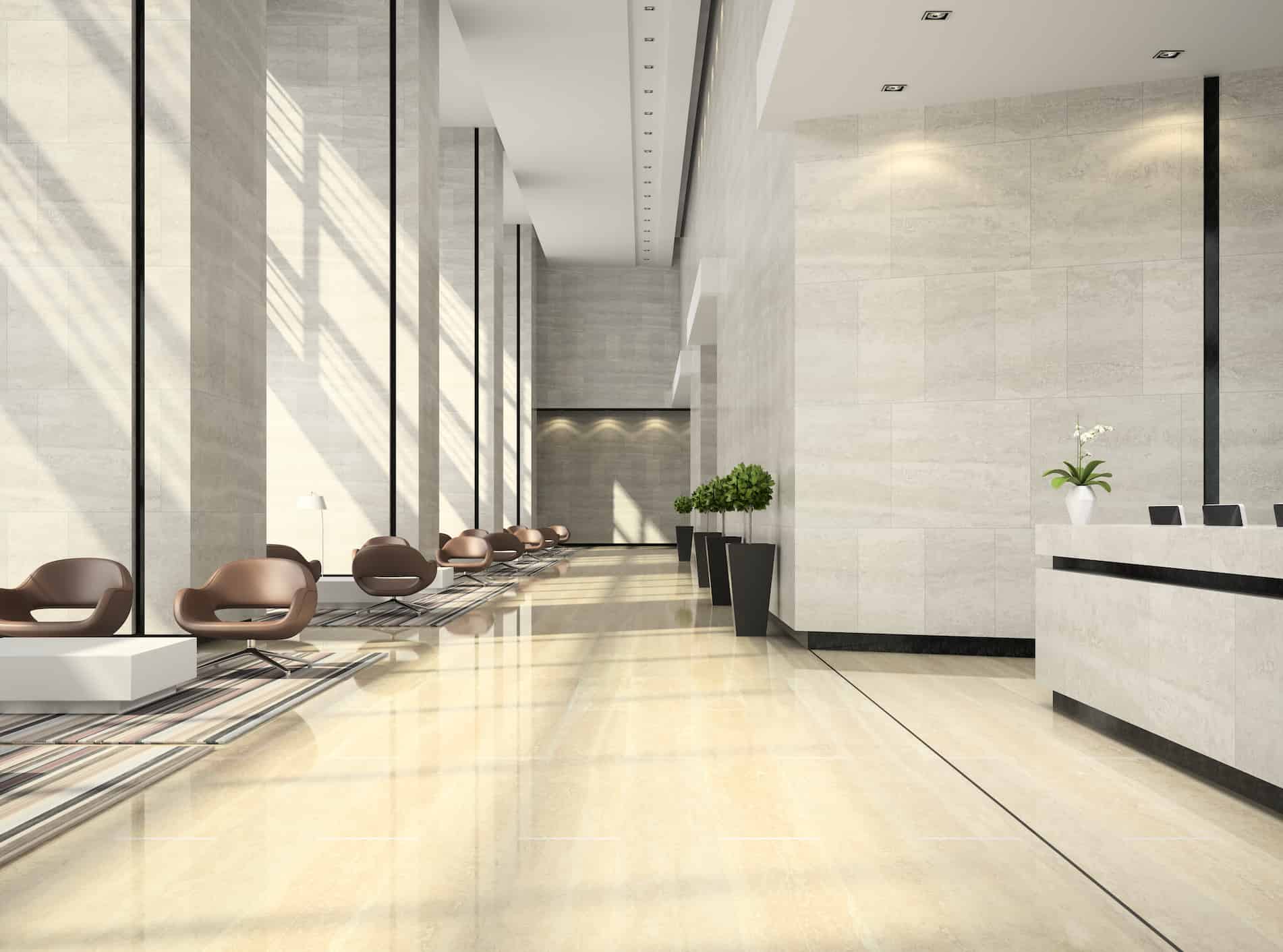 Spacious hotel lobby with modern reception desk, marble floors, lounge seating, and floor-to-ceiling windows.
